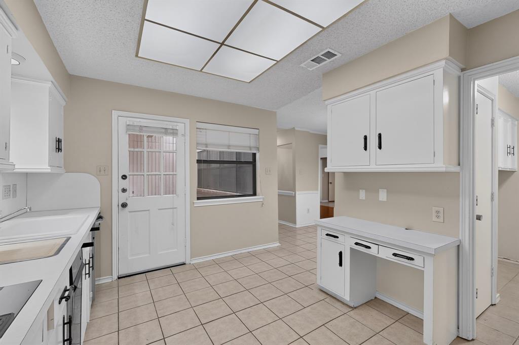 White cabinetry with black hardware, integrated desk area, tiled flooring, built-in overhead lighting, and an exterior door with glass panels