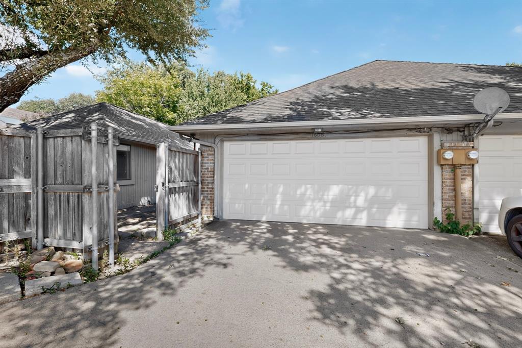 Asphalt driveway with an attached garage, brick detailing, and a separate fenced structure