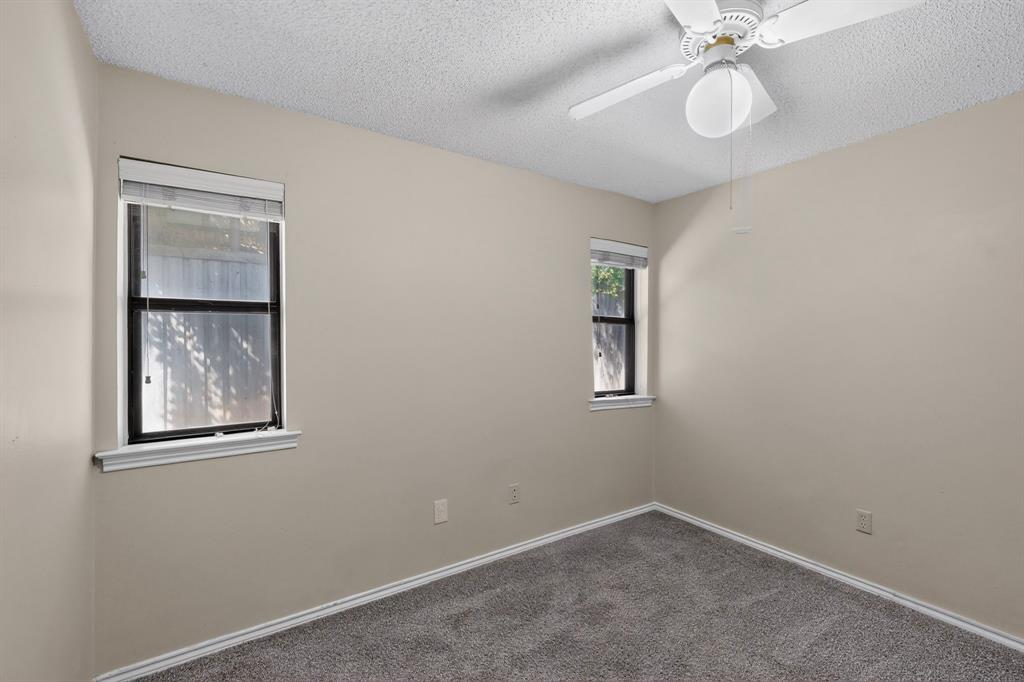 Textured ceiling with a ceiling fan light fixture, two windows with blinds, and gray carpeting