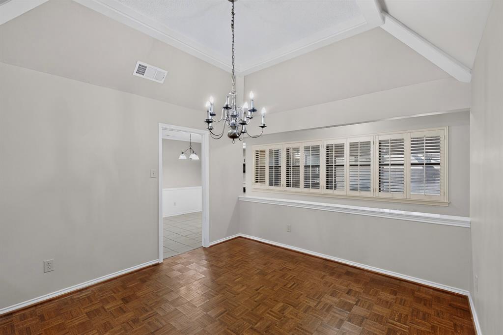 Elegant dining room showcasing soaring vaulted ceilings with crown molding, herringbone wood-finish flooring, and a striking multi-arm chandelier