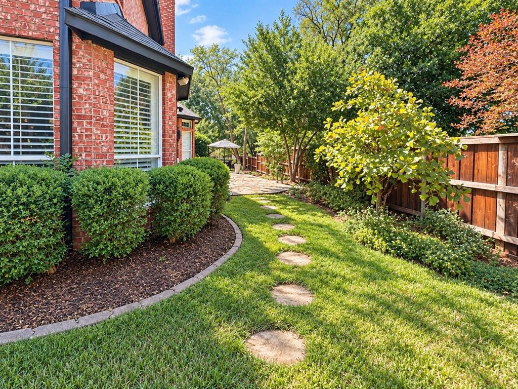 Brick exterior with white-trimmed windows, established shrubbery, a stone paver walkway, and a wooden privacy fence