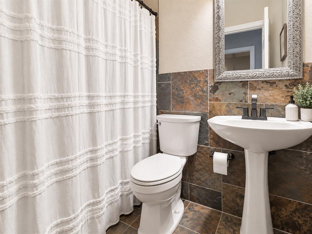 Pedestal sink with a matte black faucet, wall-mounted mirror, and multi-toned tile wainscoting