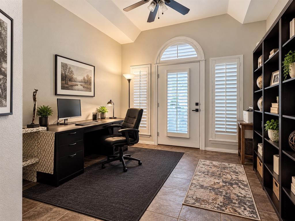 Vaulted ceiling with a ceiling fan, arched transom window, white plantation shutters, built-in shelving, and tile flooring