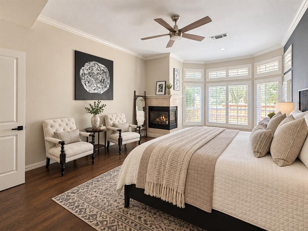 Hardwood-finish flooring, crown molding, bay windows with plantation shutters, corner fireplace with stone surround, and a ceiling fan with integrated lighting
