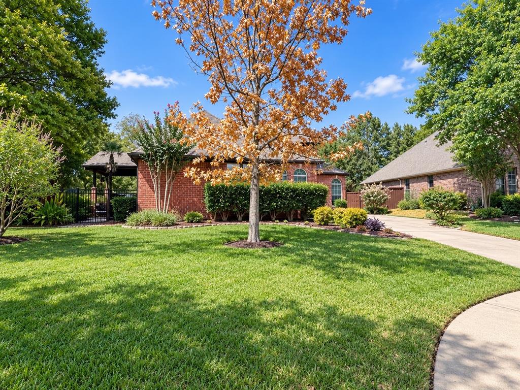Brick exterior residence with arched windows, an attached two-car garage, mature landscaping, and a fenced side yard with a pergola