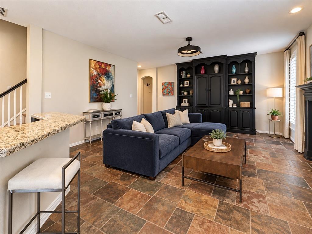 Built-in shelving unit, multi-tone tile flooring, breakfast bar with stone countertop, staircase with white spindles, and window with plantation shutters