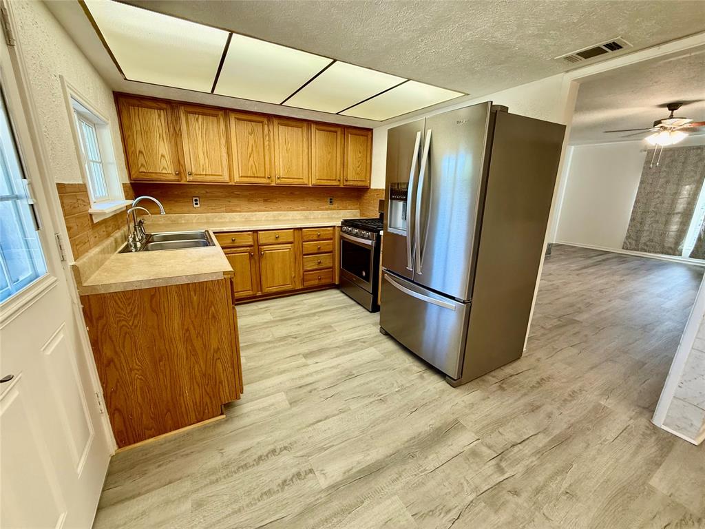Kitchen featuring wood cabinetry, stainless steel refrigerator, stainless steel range, and wood-finish flooring Kitchen featuring wood cabinetry, stainless steel refrigerator, stainless steel range, and wood-finish flooring