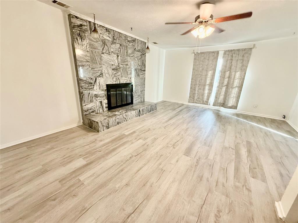 Spacious interior with light wood-finish flooring, a stone-clad fireplace with hearth, and a ceiling fan with integrated lighting Spacious interior with light wood-finish flooring, a stone-clad fireplace with hearth, and a ceiling fan with integrated lighting