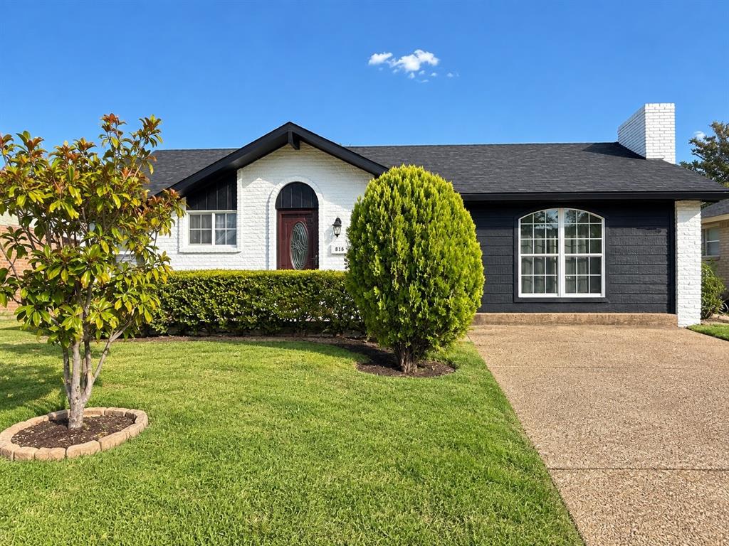 White brick exterior with dark shingle roofing, an arched entryway, a prominent arched window, and a light-colored driveway White brick exterior with dark shingle roofing, an arched entryway, a prominent arched window, and a light-colored driveway