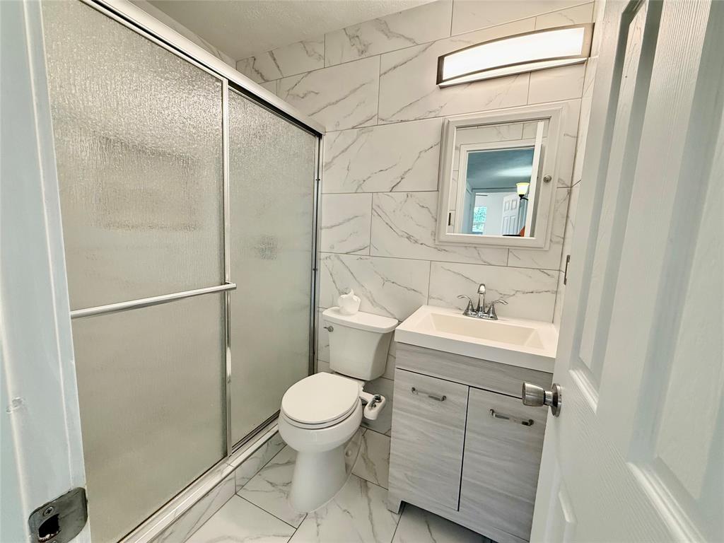 Full-height tiled walls featuring a white marble-look pattern, white vanity with integrated sink, chrome faucet, and a sliding glass shower enclosure Full-height tiled walls featuring a white marble-look pattern, white vanity with integrated sink, chrome faucet, and a sliding glass shower enclosure