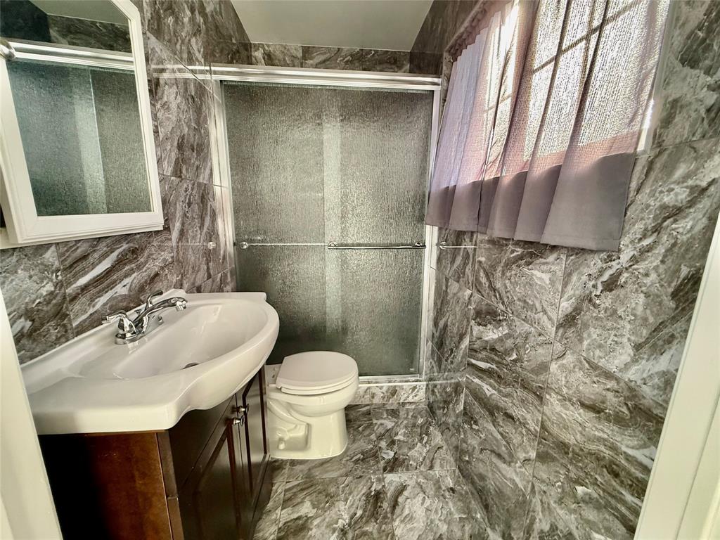 Tiled walls and flooring, wood-finish vanity with an integrated sink, polished chrome faucet, and a sliding glass shower enclosure Tiled walls and flooring, wood-finish vanity with an integrated sink, polished chrome faucet, and a sliding glass shower enclosure