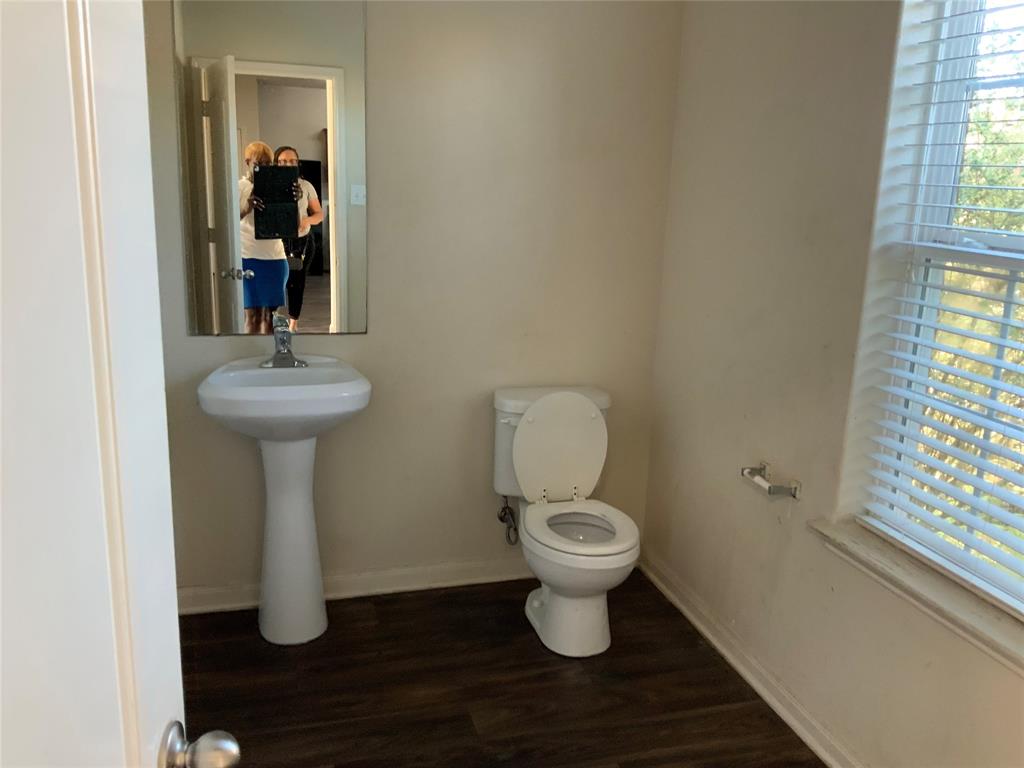 Pedestal sink with mirror, toilet, and wood-finish flooring Pedestal sink with mirror, toilet, and wood-finish flooring