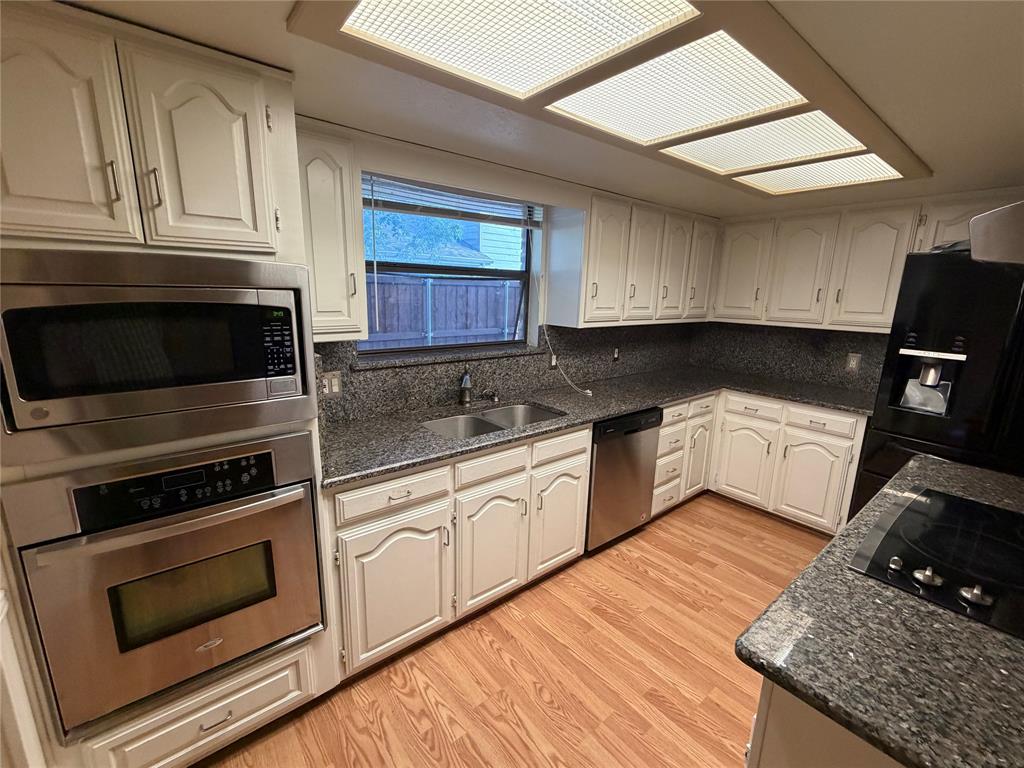 Kitchen featuring white cabinetry, dark stone countertops, stainless steel appliances, and wood-finish flooring
