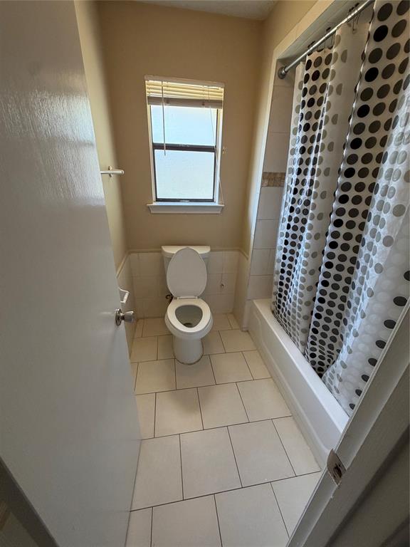 White tile flooring, a window with blinds, a built-in bathtub, and ceramic wall tiling