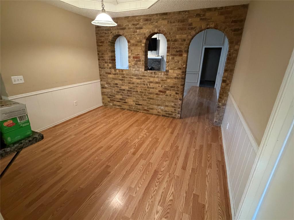 Hardwood-finish flooring, brick accent wall with arched openings, white paneled wainscoting, and a built-in ceiling light fixture