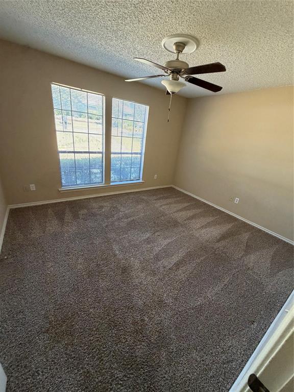 Spacious room featuring neutral carpeting, two large windows with blinds, a ceiling fan with integrated lighting, and textured ceilings