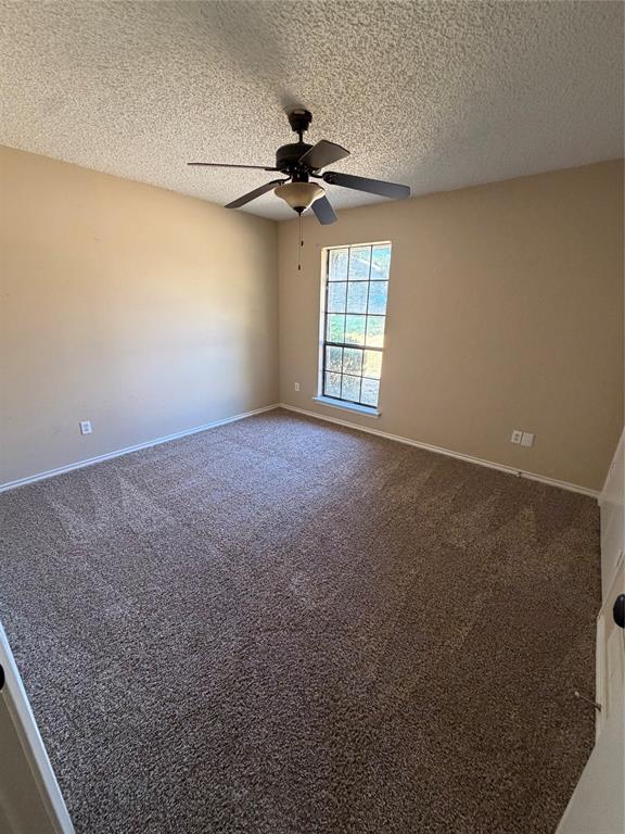 Carpeted room featuring neutral-toned walls, a single window with a white frame, and a ceiling-mounted fan with integrated lighting