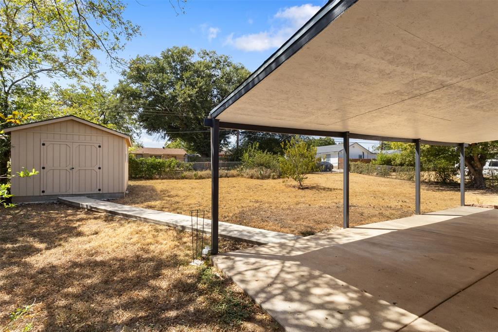 Expansive backyard featuring a covered patio, concrete walkway, and a detached storage shed