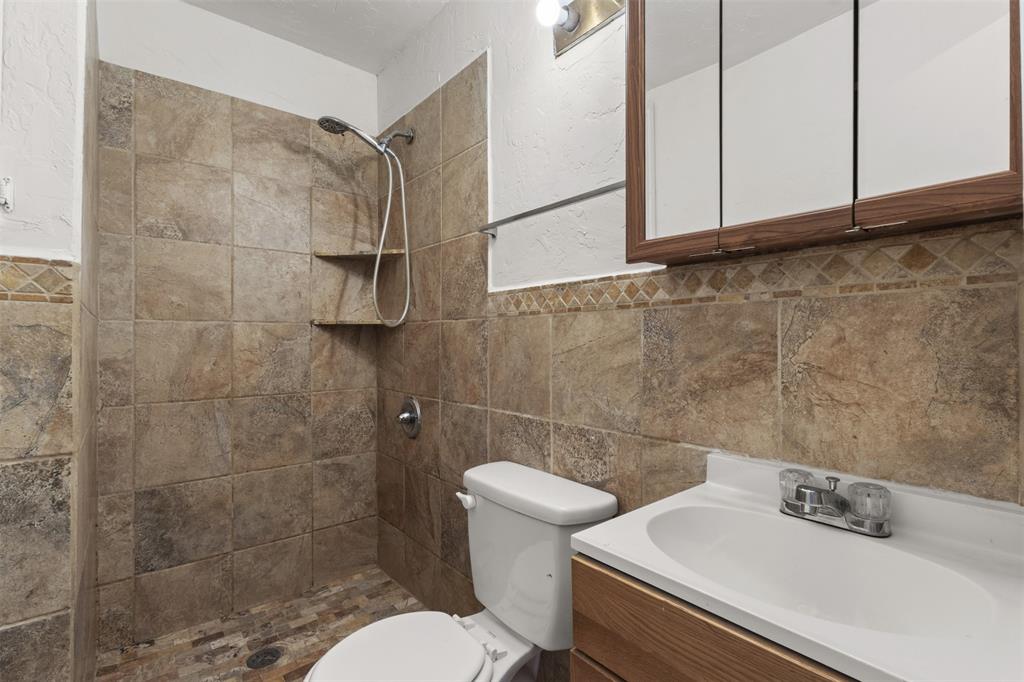 Tiled shower with built-in shelving, a vanity with an integrated sink, a medicine cabinet, and a decorative tile accent band