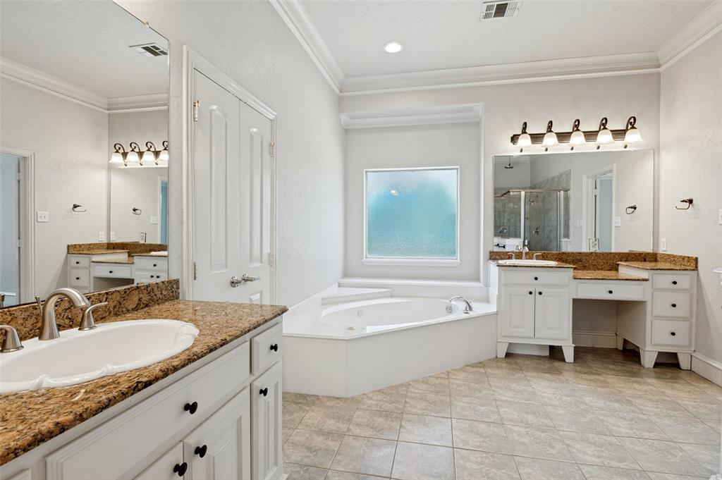 Spacious bathroom featuring dual vanities with stone countertops, a built-in soaking tub, a large tiled shower, and tile flooring
