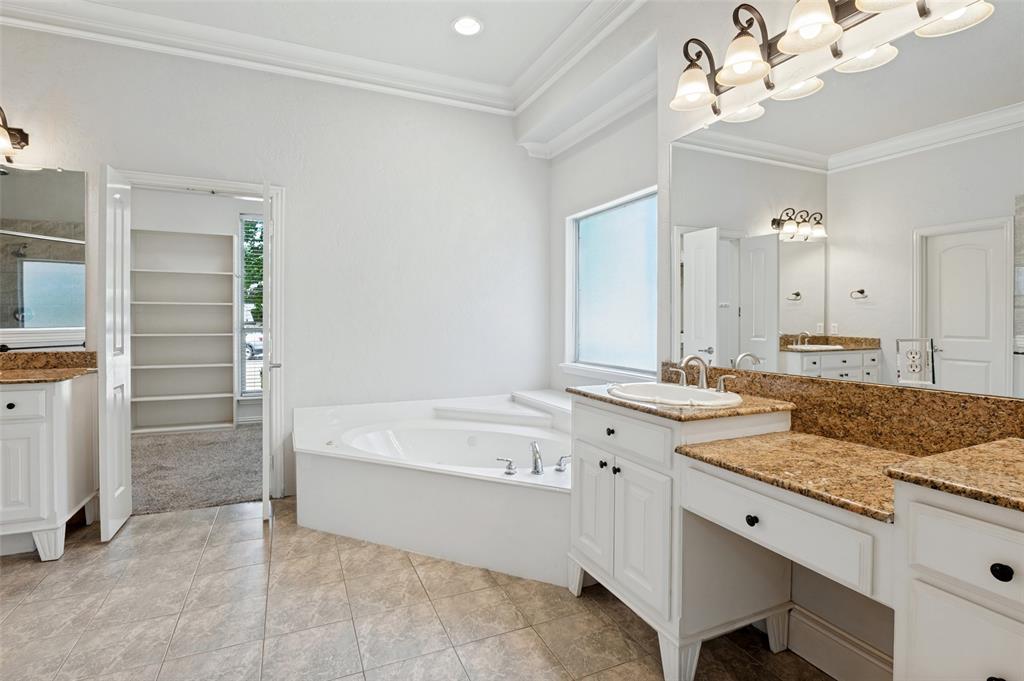 Bathroom featuring dual vanities with stone countertops, a built-in corner soaking tub, tile flooring, and crown molding