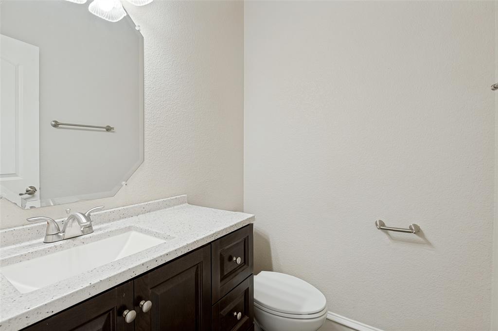 Dark wood-finish vanity with an integrated sink, light-toned countertop, brushed nickel faucet, and an octagonal mirror
