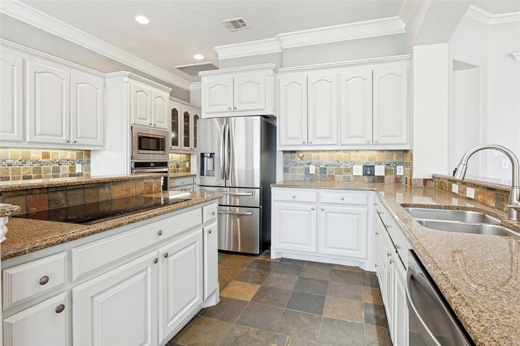 White cabinetry, stainless steel appliances, stone tile flooring, granite countertops, and a decorative tile backsplash