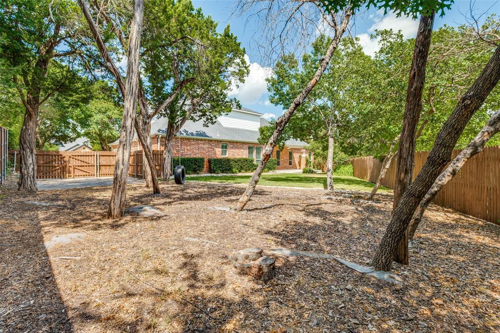 Expansive backyard with multiple mature trees, a wood privacy fence, and a brick exterior dwelling visible in the background