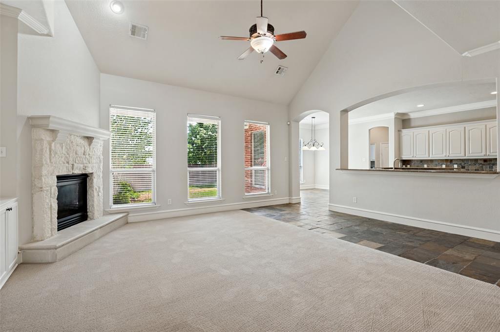 Vaulted ceilings, a stone-clad fireplace, and a ceiling fan enhance the living area, while a breakfast bar with white cabinetry and a tile backsplash separates the kitchen space