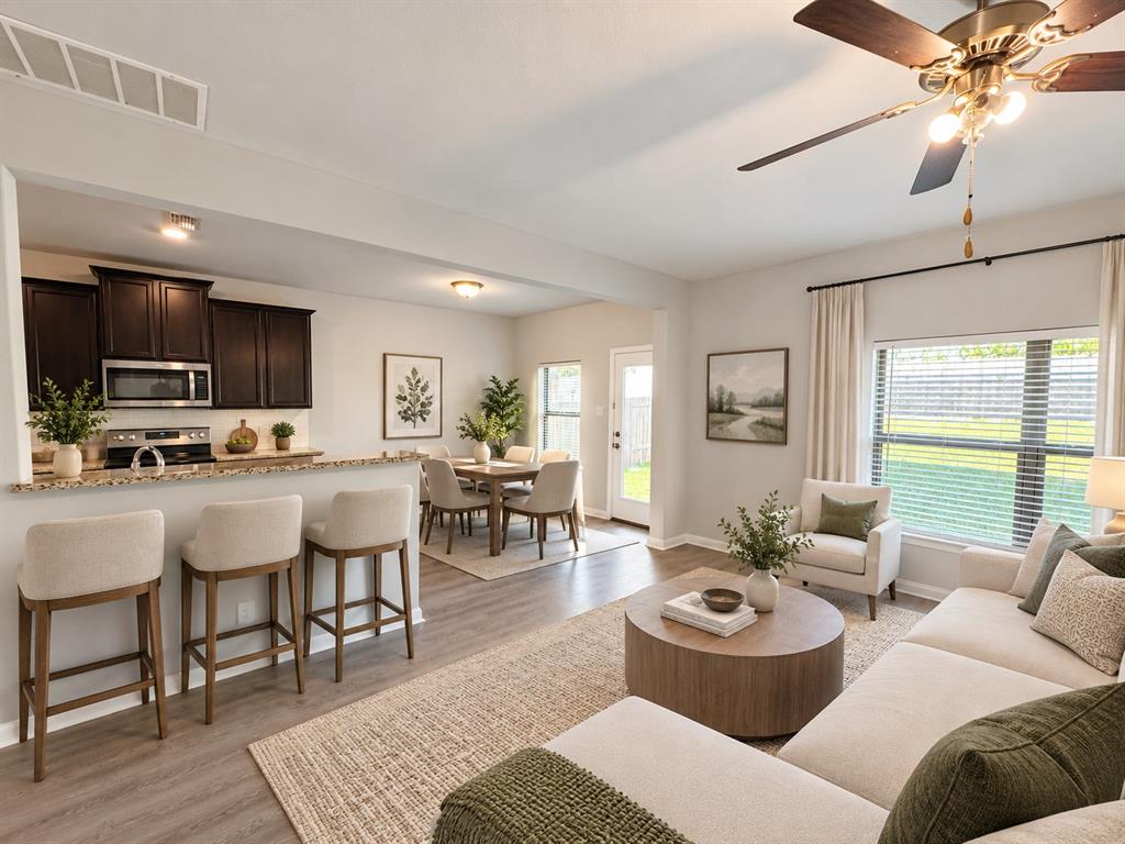 Open-concept living space featuring wood-finish flooring, a kitchen island with stone-finish countertop, dark wood cabinetry, and a ceiling fan with integrated lighting Open-concept living space featuring wood-finish flooring, a kitchen island with stone-finish countertop, dark wood cabinetry, and a ceiling fan with integrated lighting