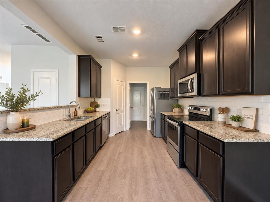 Wood-finish flooring, dark wood cabinetry, light-toned countertops, white subway tile backsplash, and stainless steel appliances Wood-finish flooring, dark wood cabinetry, light-toned countertops, white subway tile backsplash, and stainless steel appliances