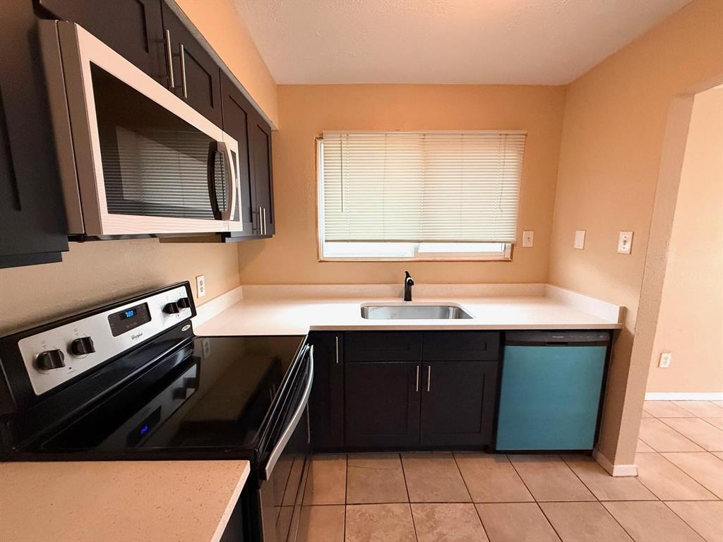 Kitchen featuring dark wood-finish cabinetry, light-toned countertops, tile flooring, and stainless steel appliances