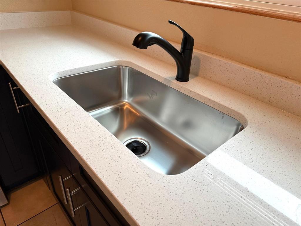 Undermount stainless steel sink with a matte black faucet, set within a light-toned countertop with integrated backsplash