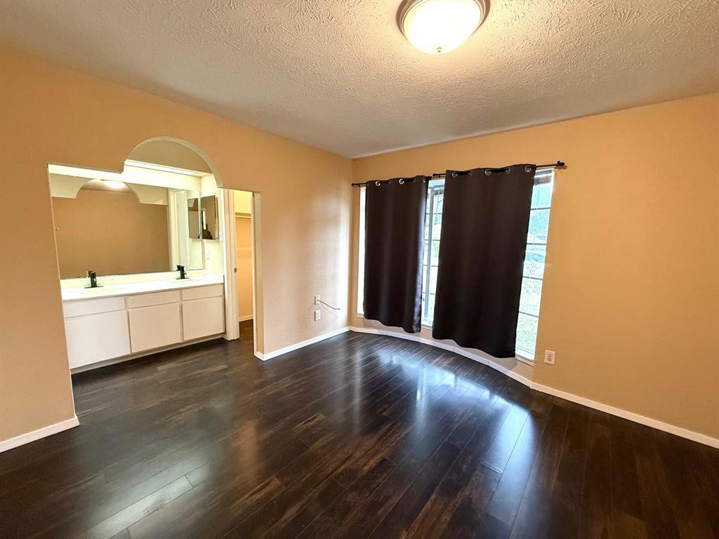Wood-finish flooring throughout, featuring a curved bay window, and an arched entry to a double vanity with two mirrors