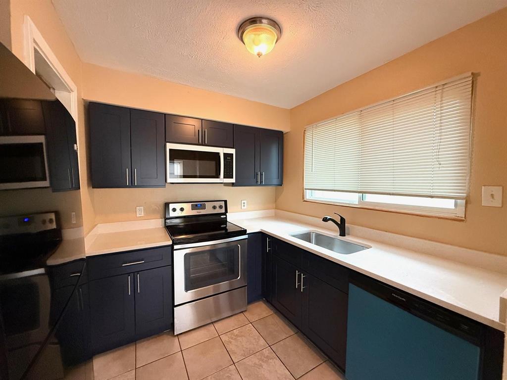 Galley kitchen featuring dark blue cabinetry, stainless steel appliances, light-toned countertops, and tile flooring