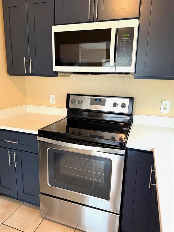 Stainless steel electric range with a smooth cooktop, stainless steel microwave, dark cabinetry with bar pull hardware, and light-toned countertops