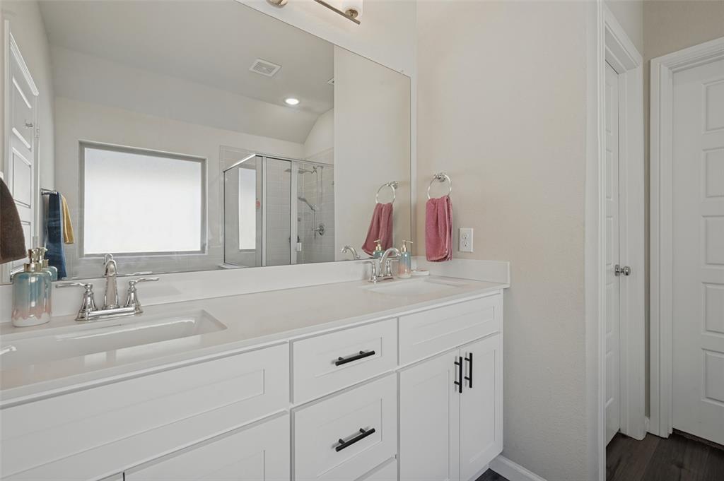 Dual vanity with white cabinetry and dark hardware, integrated sinks, chrome fixtures, and a large wall-mounted mirror