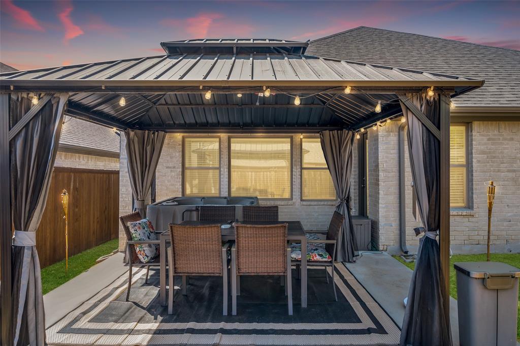 Patio area featuring a dark metal gazebo with string lighting, privacy curtains, and concrete hardscaping
