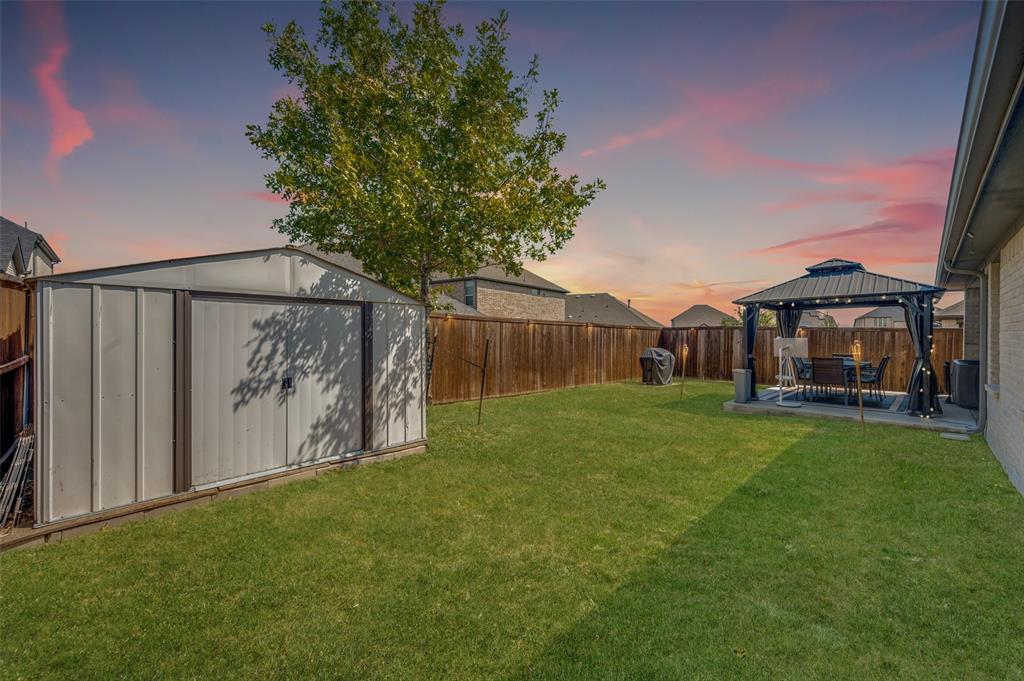 Expansive backyard with a metal storage shed, wood fence, and a patio area featuring a gazebo