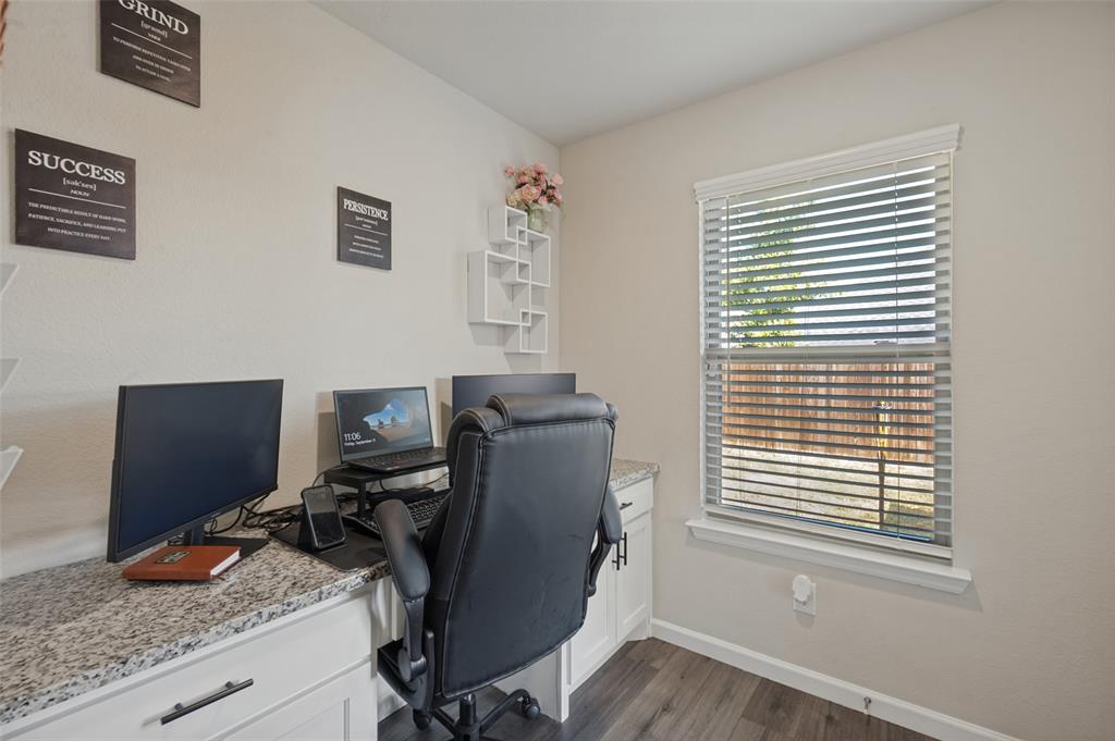 Dedicated home office featuring a wood-finish desk with quartz countertop, ergonomic seating, dual monitor setup capability, and abundant natural light from a large window with plantation shutters