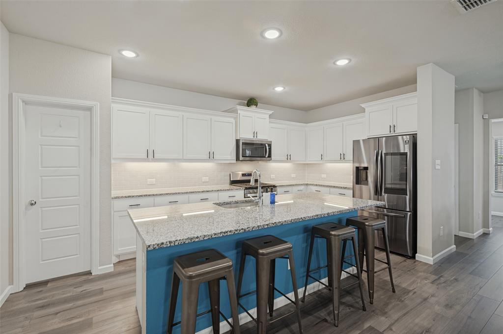 Kitchen featuring an expansive island with a blue base and light-colored countertop, white upper and lower cabinetry, stainless steel appliances, and wood-finish flooring Kitchen featuring an expansive island with a blue base and light-colored countertop, white upper and lower cabinetry, stainless steel appliances, and wood-finish flooring