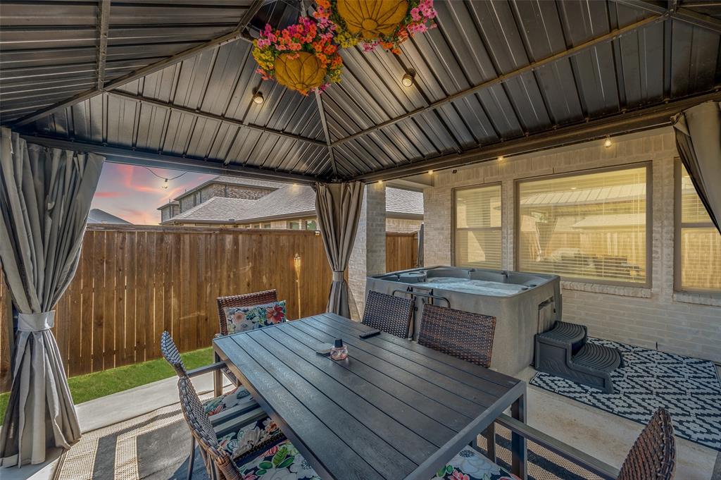Covered patio with a metal roof and string lighting, featuring a built-in hot tub, concrete patio, and a privacy fence