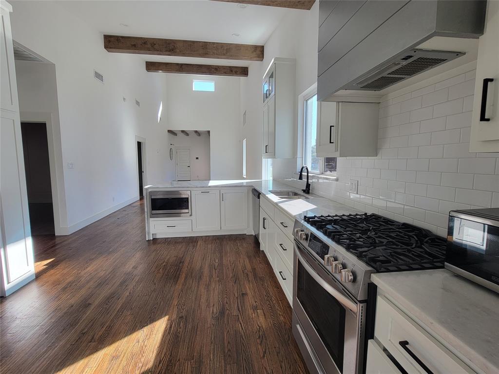 Kitchen featuring wood-finish flooring, vaulted ceilings with exposed wood beams, white cabinetry, subway tile backsplash, and a gas range