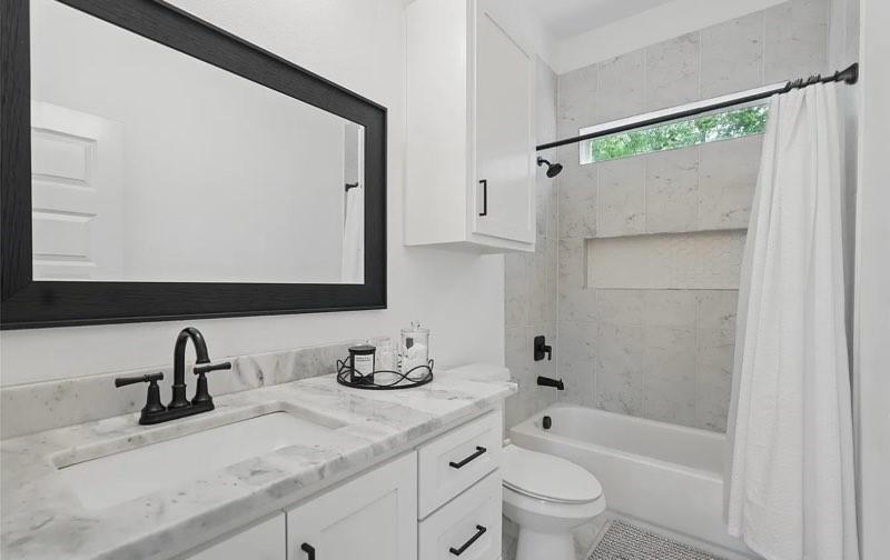 Bathroom featuring a white vanity with stone-top surfacing, undermount sink, matte black hardware, tiled shower surround with an integrated wall niche, and a framed mirror