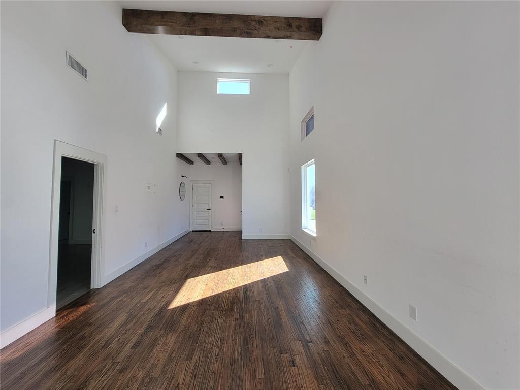 Vaulted ceiling featuring exposed wood beams, wood-finish flooring, and multiple natural light sources