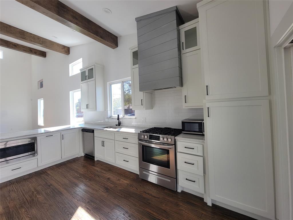 Kitchen featuring exposed timber ceiling beams, shaker-style cabinetry, a custom range hood, and stainless-steel appliances atop wood-finish flooring