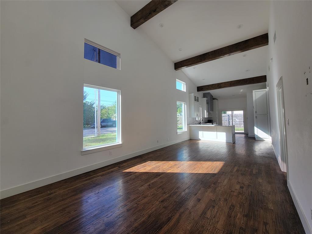 Vaulted ceilings with exposed structural beams, wood-finish flooring, and multiple oversized windows providing natural light