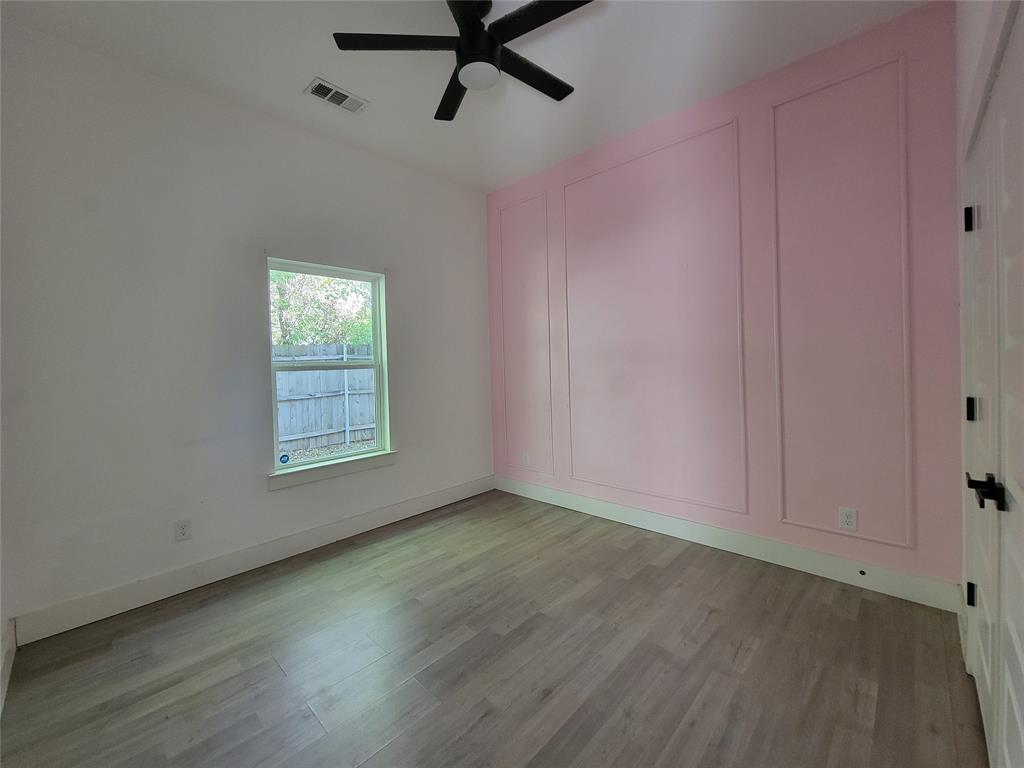 Room featuring wood-finish flooring, decorative wall molding, a window, and a ceiling fan with integrated lighting