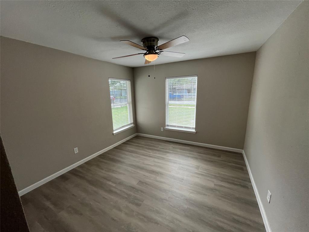 Neutral-toned walls, wood-finish flooring, dual windows with blinds, and a central ceiling fan with an integrated light fixture