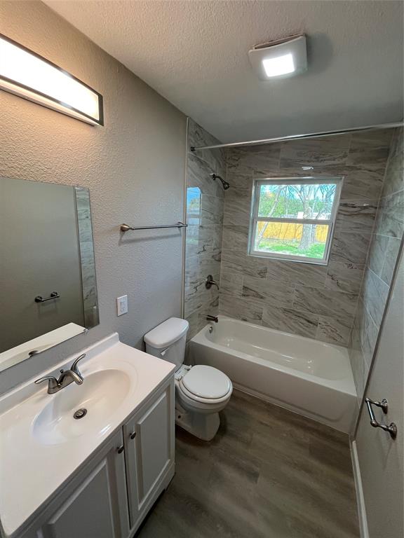 Bathroom featuring a white vanity with a composite countertop, wood-finish flooring, shower-tub combination with horizontal tile surround, and a wall-mounted LED vanity light
